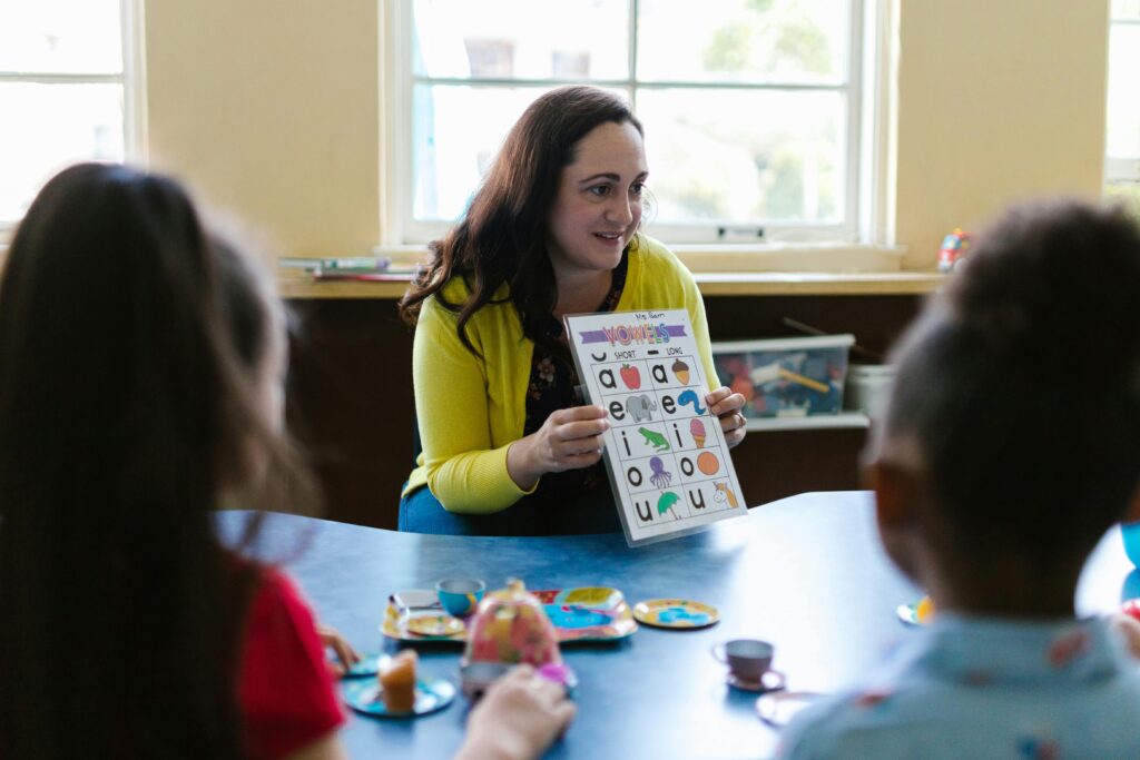 Teacher engaging young children in a fun learning activity with phonics chart in a classroom setting.