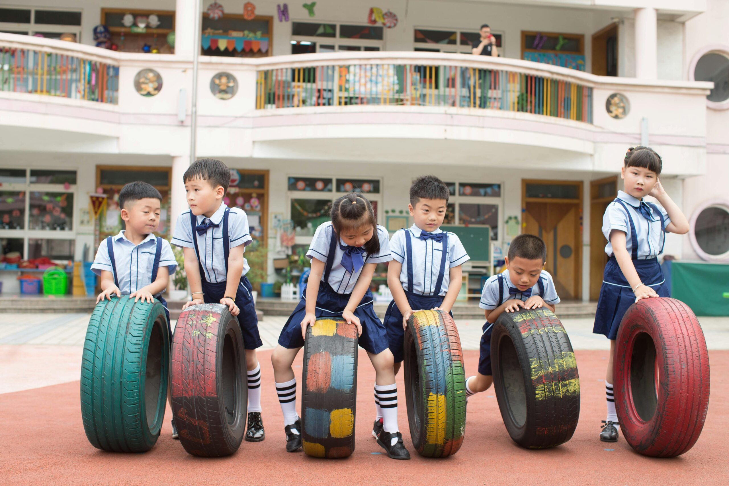Young children in uniform play with colorful tires in a school playground.