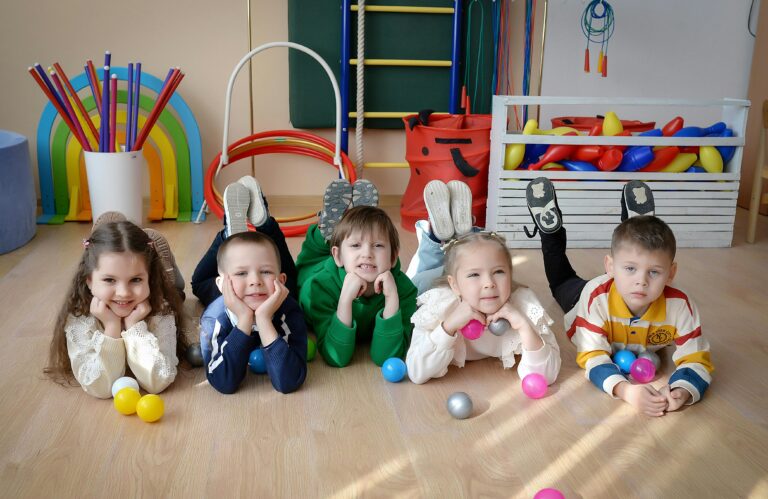 Five children happily playing with colorful balls in a vibrant indoor playroom.